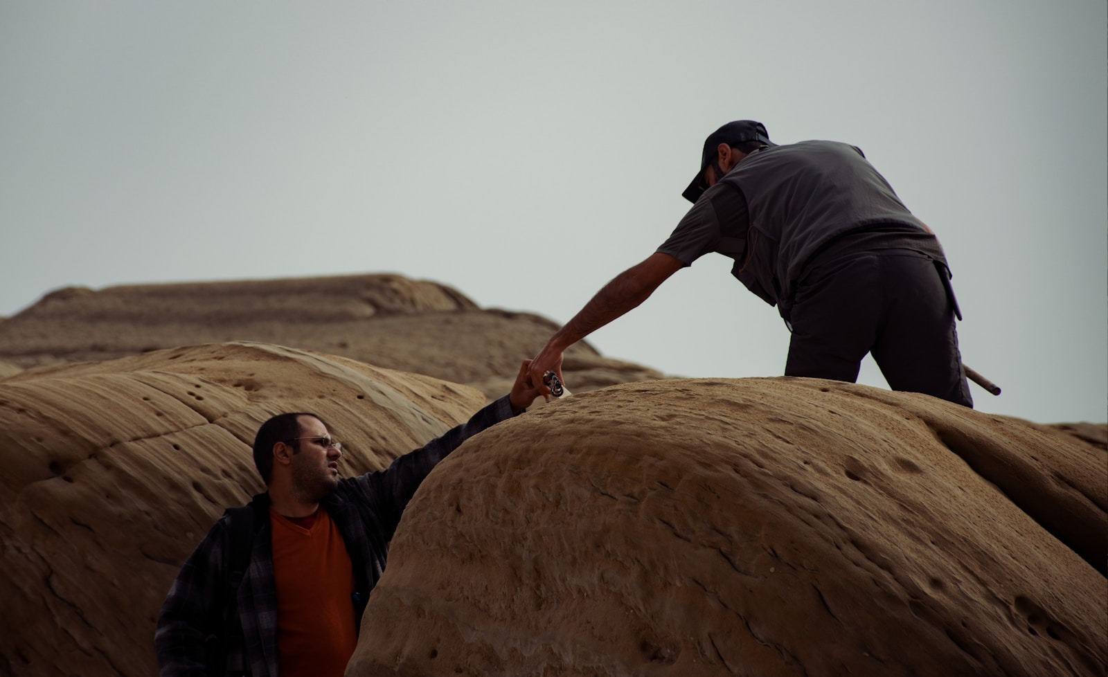 a man reaching out his hand to another man on top of a rock