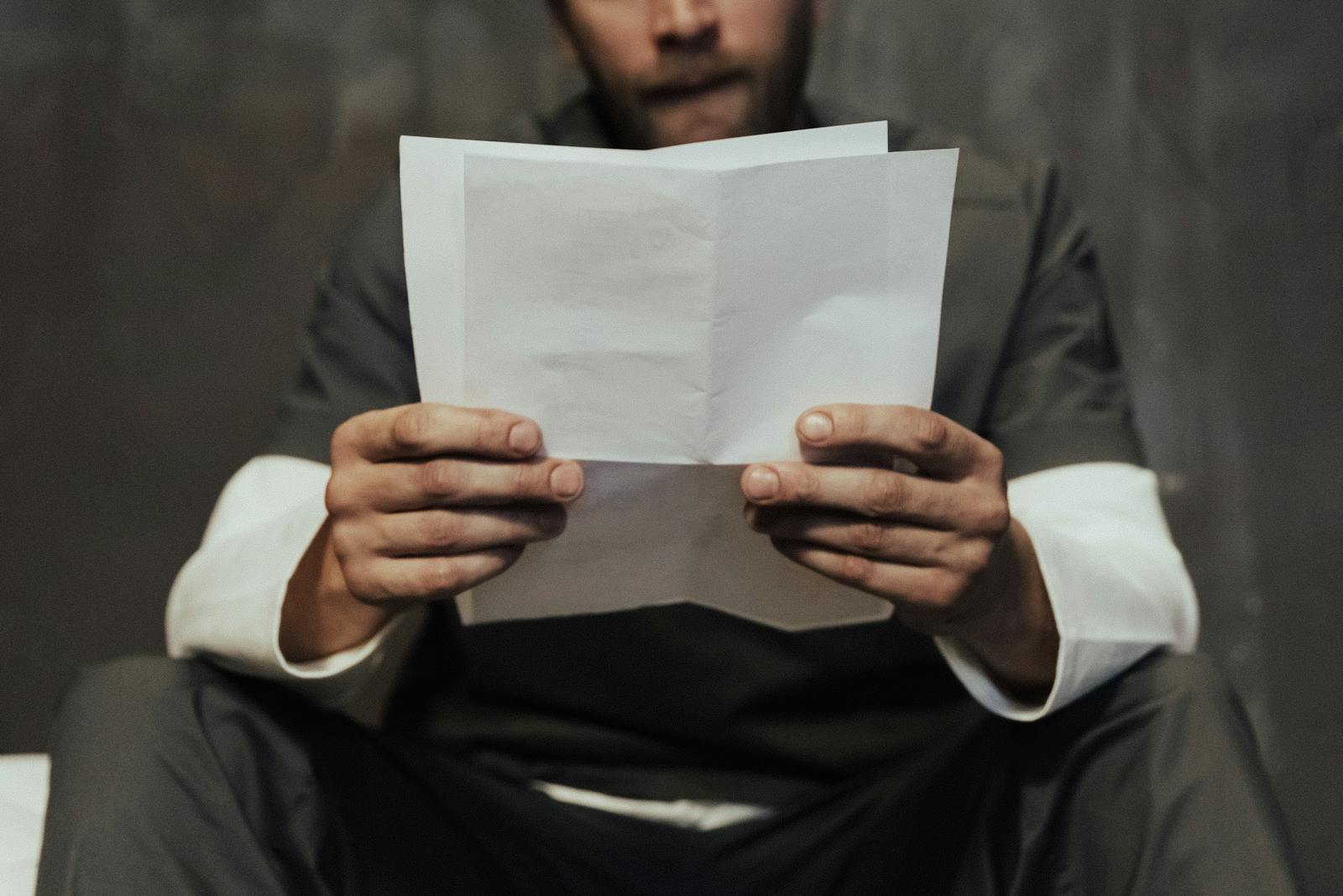 Close-up of a prisoner in uniform reading a letter in a cell setting, highlighting prison life.